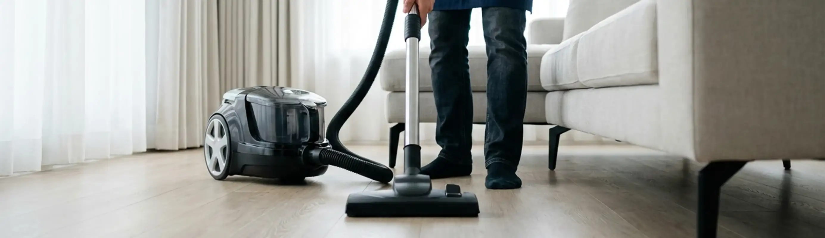 Professional house cleaner vacuuming a living room floor with a canister vacuum cleaner, Green Bay, WI.