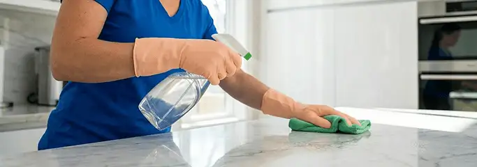 Maid service worker spraying and wiping a kitchen countertop with a microfiber cloth for sanitizing, Green Bay, WI.