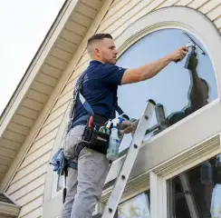 Professional window cleaner on a ladder using a squeegee to clean an exterior arched window, Green Bay, WI.