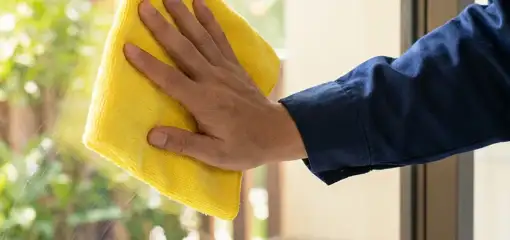 House cleaner wiping a glass window with a yellow microfiber cloth for streak-free cleaning, Green Bay, WI.